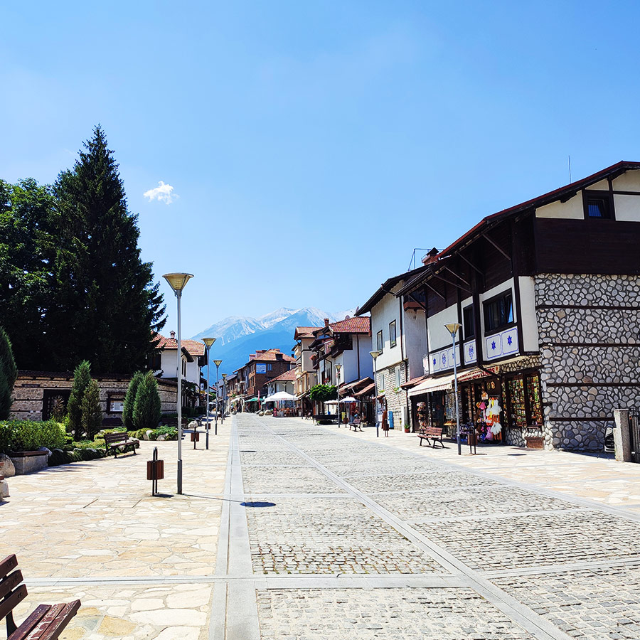 Traditional houses and cobbled street in Bansko old town with Pirin Mountains in the background, Bulgaria.