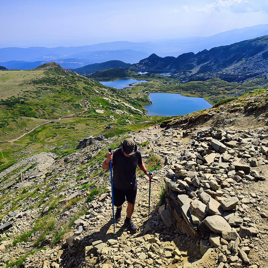 Hiker ascending rocky trail with lakes in the background, Seven Rila Lakes, Bulgaria.