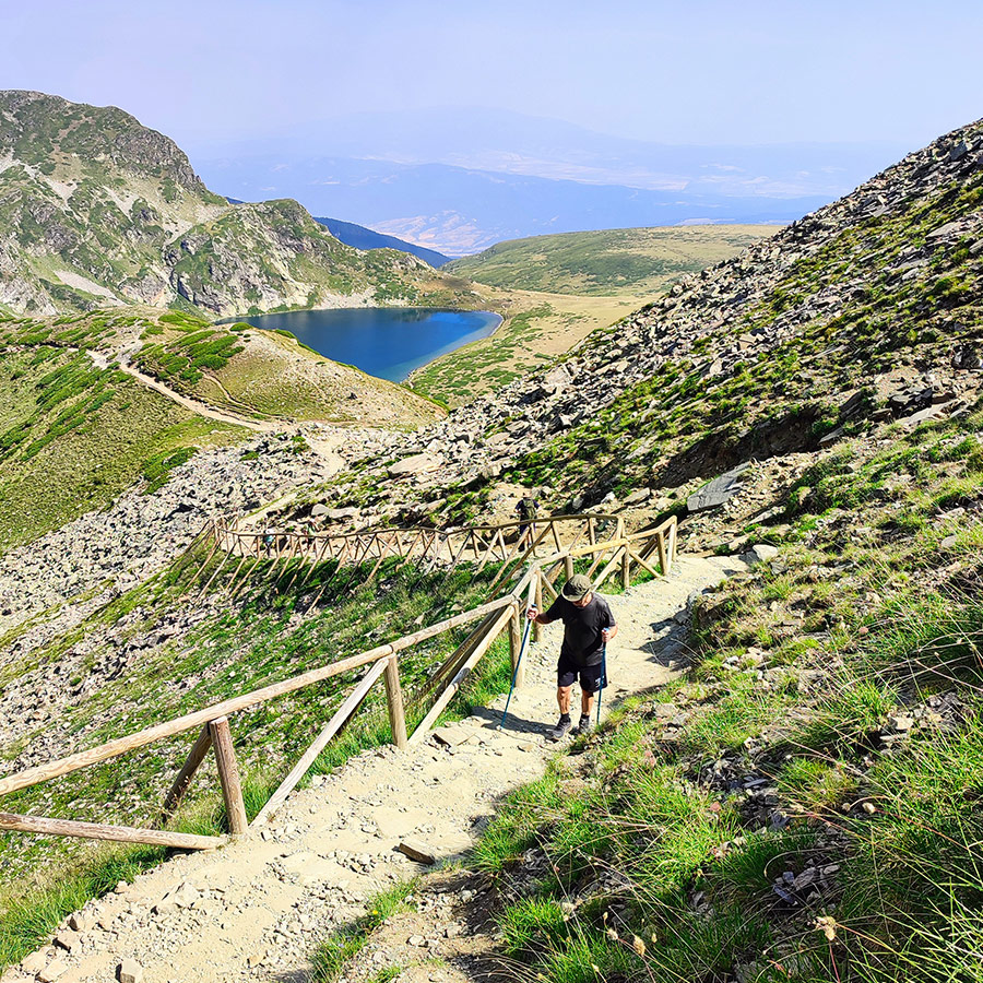 Hiker ascending wooden steps with alpine lake in the background, Seven Rila Lakes, Bulgaria.