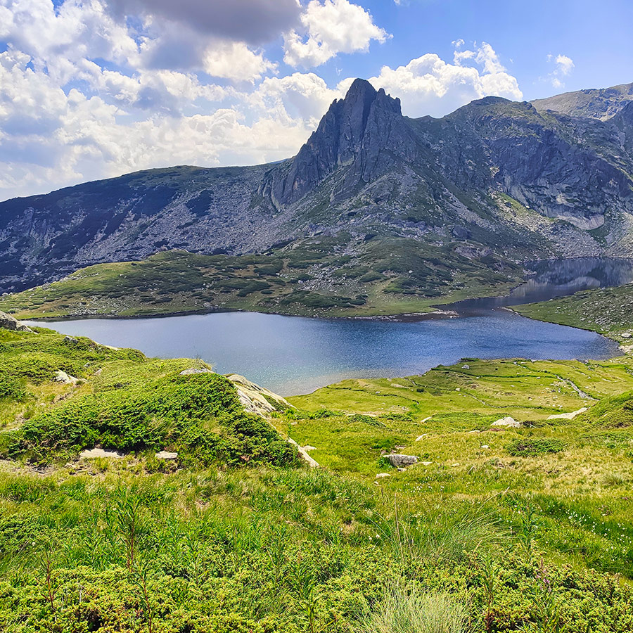 Scenic alpine lake beneath a sharp rocky peak in Rila Mountain.