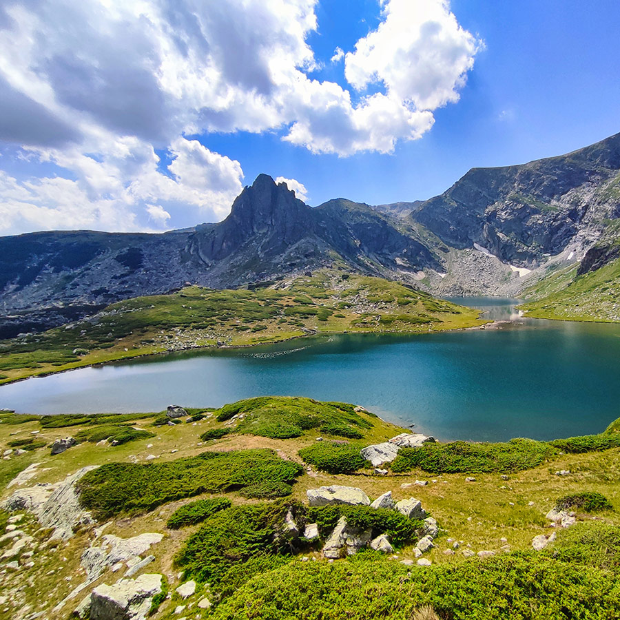Alpine lake surrounded by green meadows and jagged peaks in Rila Mountain.