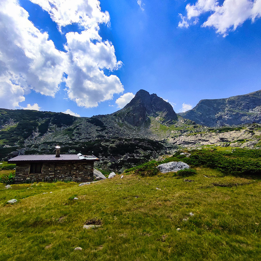 Traditional stone mountain hut with alpine peaks in the background.