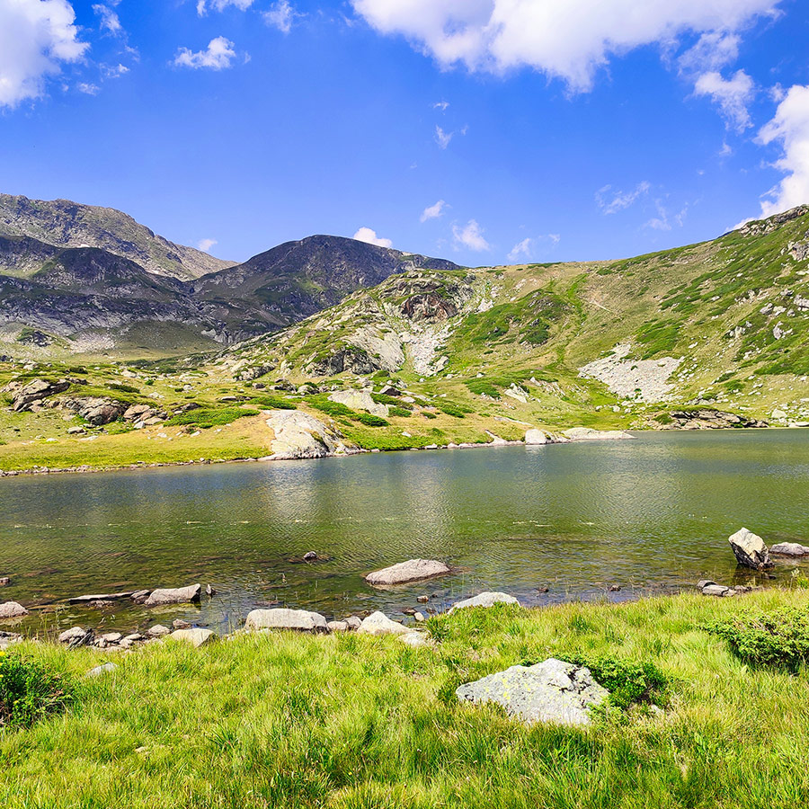 Calm alpine lake reflecting mountain slopes and blue skies in Rila Mountain.