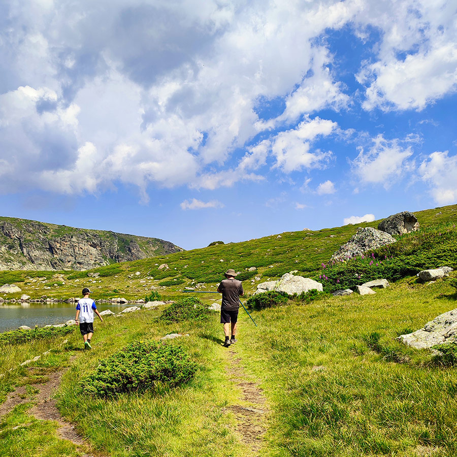 Hikers walking along a grassy trail by one of the Seven Rila Lakes.