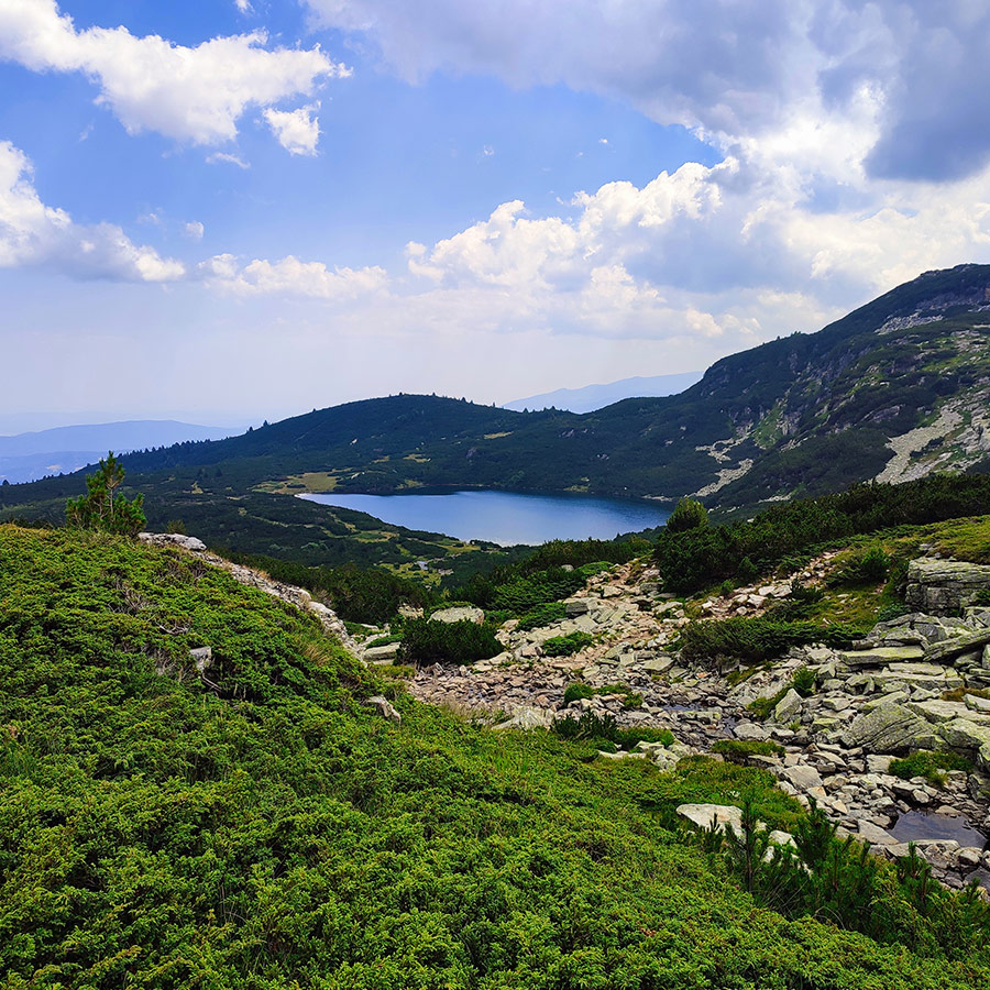 View of the Kidney Lake from above, surrounded by green ridges and alpine slopes.