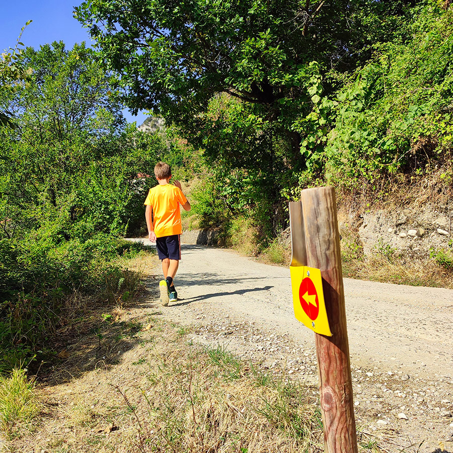 Hiker on forest road with trail sign pointing to Anthochori Waterfall, Agrafa, Karditsa, Greece