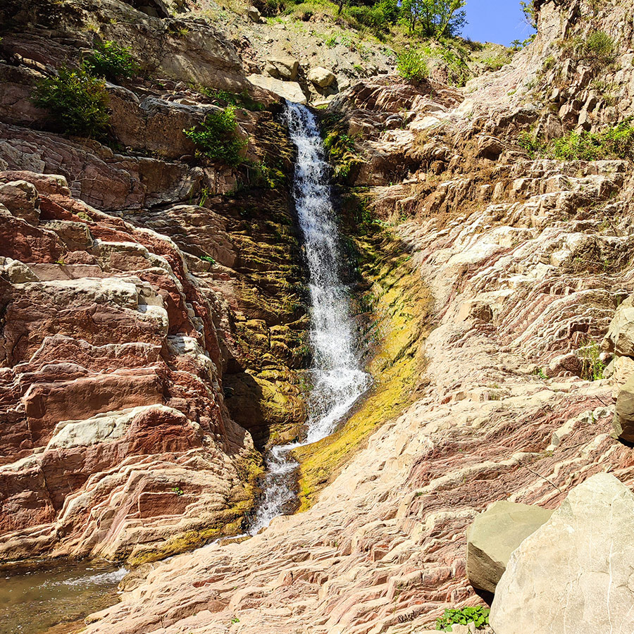 Anthochori Waterfall surrounded by layered red and yellow rocks in Agrafa, Greece