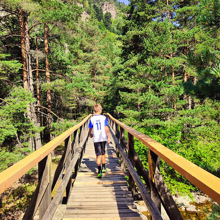 Child walking across a wooden bridge with mountain views on the Beli Iskar Eco Trail.