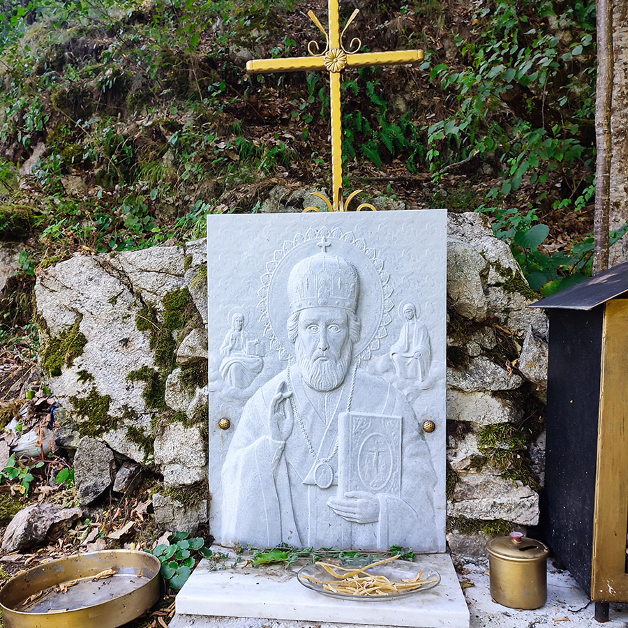 Stone shrine of Saint Nicholas with golden cross near the waterfall in Bansko, Bulgaria.