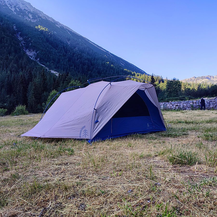 Sierra Designs Flash 3 tent in an open meadow with Pirin Mountain peaks in the background.
