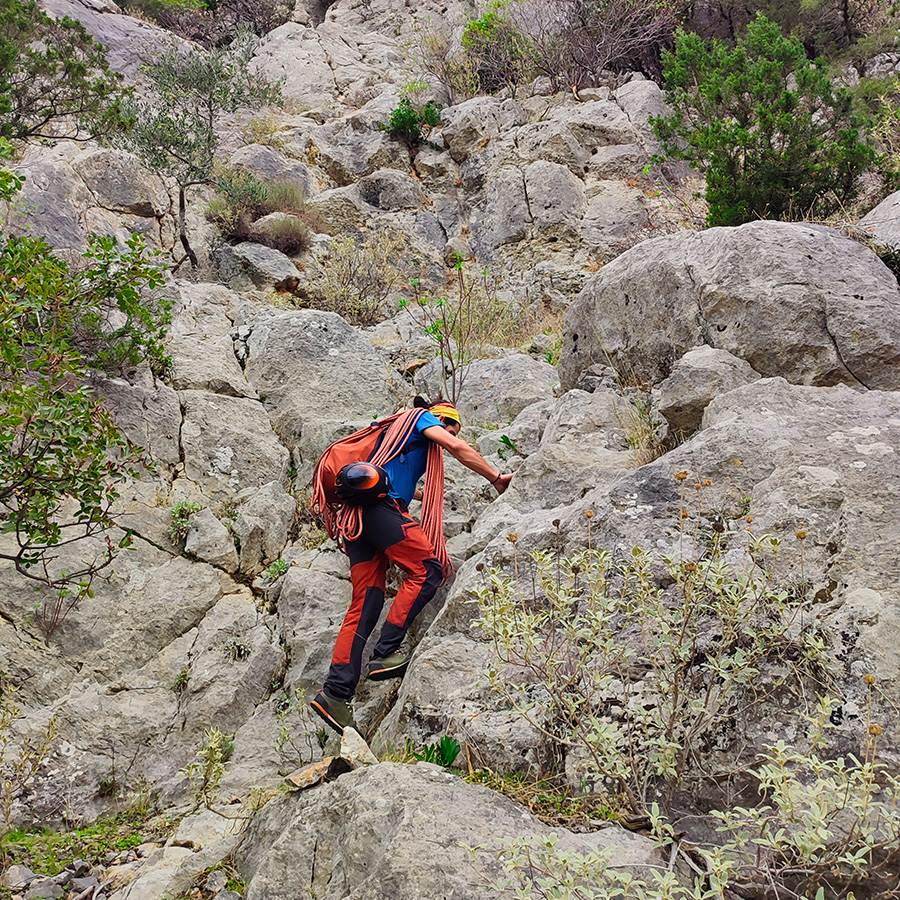 Climber scrambling over limestone terrain to reach the starting ledge of the Asterope route.