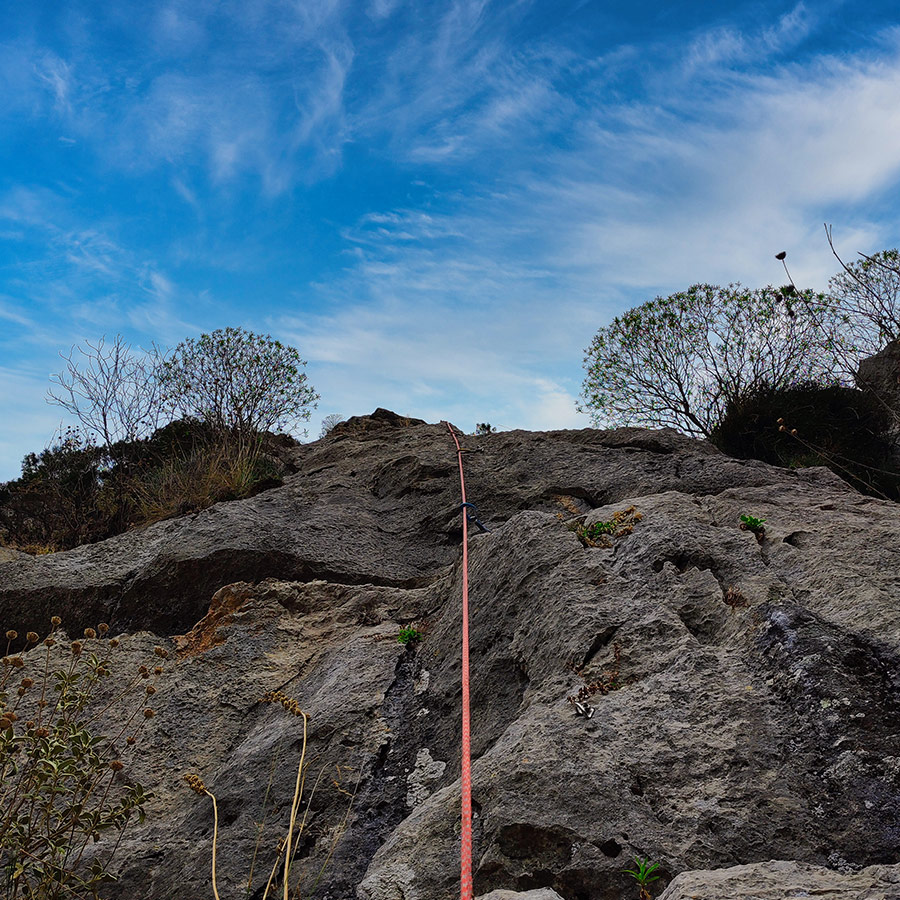 Red climbing rope clipped into bolts on limestone slab of Asterope’s upper section.