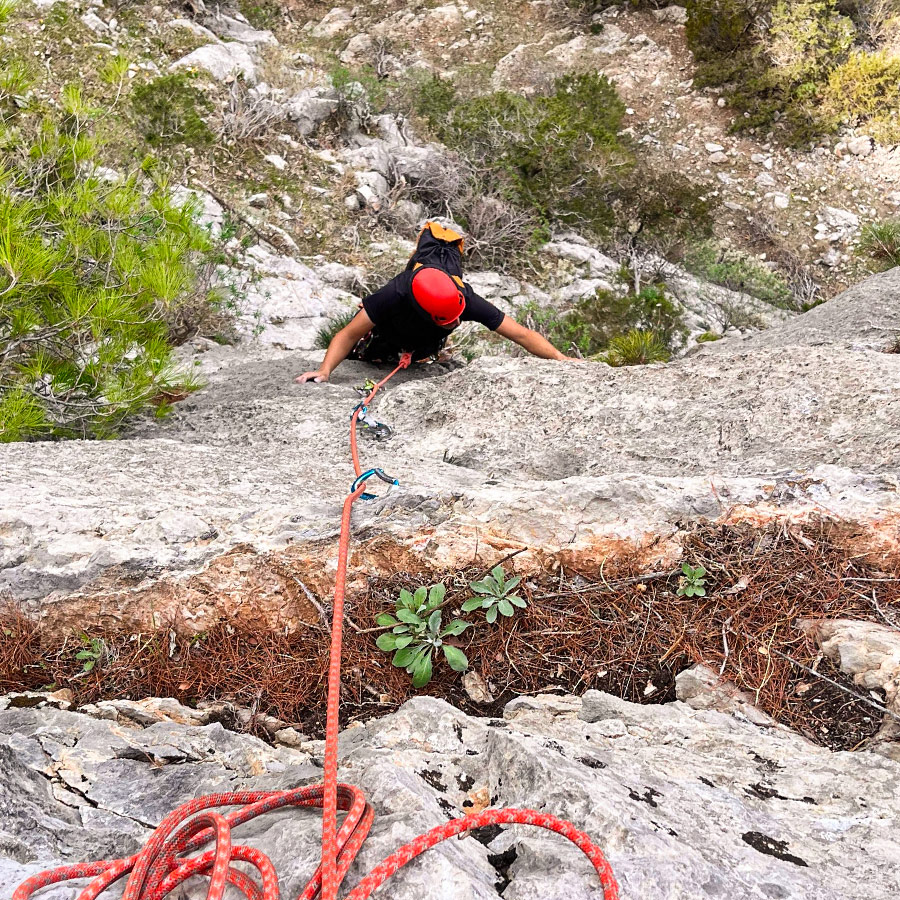 Climber reaching upper moves of Asterope route with red rope trailing below.