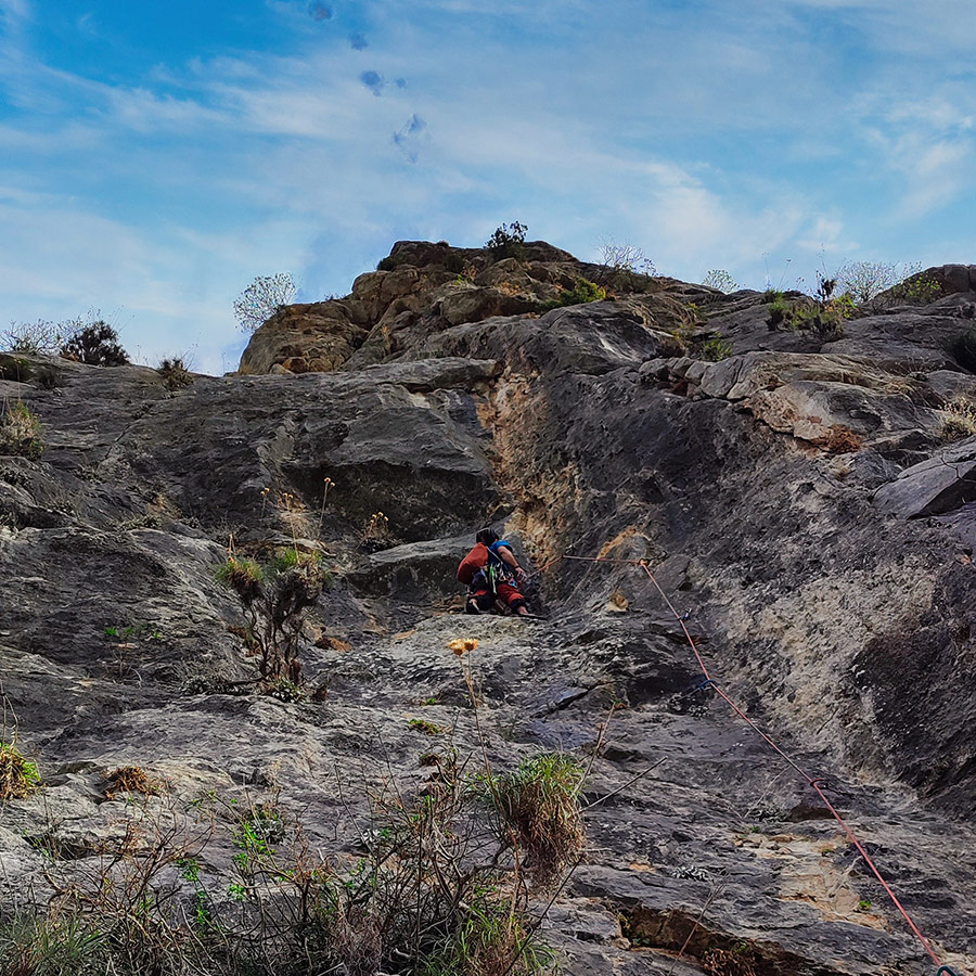 Climber tackling steep upper section of Asterope route under bright sky.