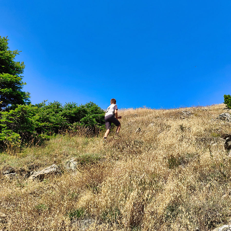 Young hiker climbing the final grassy slope to Voulgara Peak in the Agrafa Mountains.